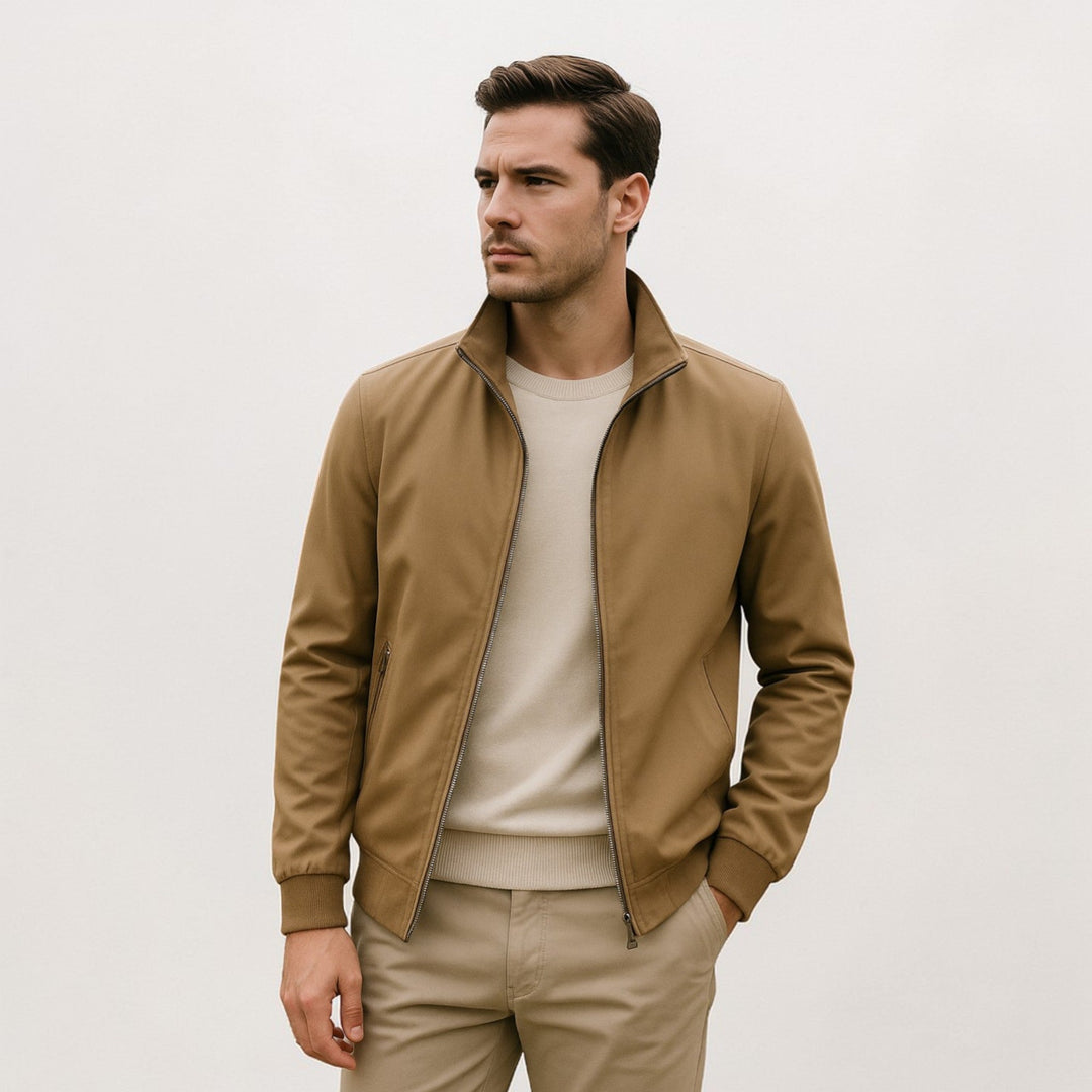 Model in the tan jacket with stand collar and ribbed hem, worn open over a cream sweater with one hand in pocket. 4