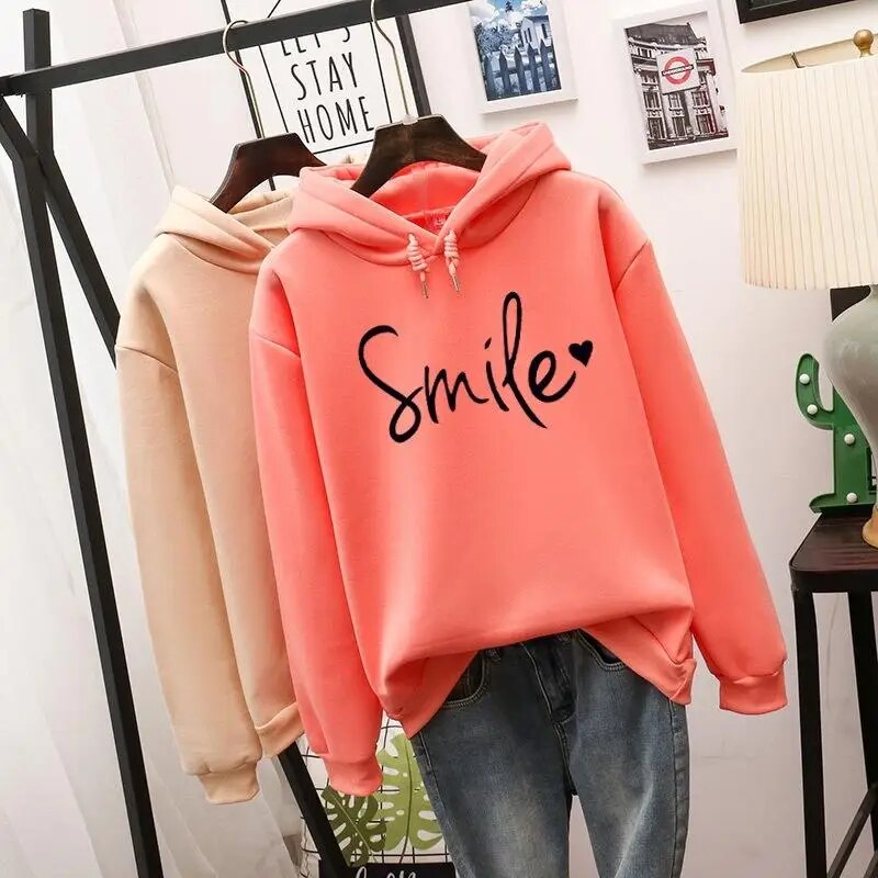 Coral-orange hoodie in front with a beige hoodie behind it on a rack, both showing the same black script print.