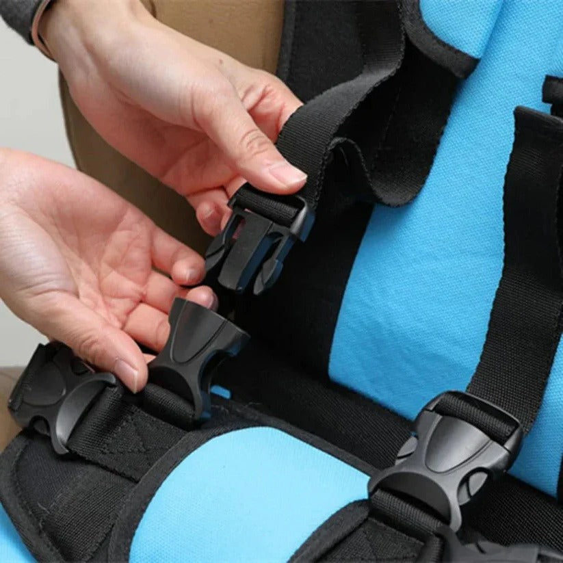 Close-up of hands unclipping a black plastic buckle on the blue travel seat's harness straps.