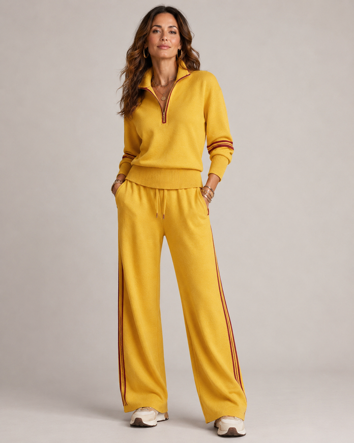 Woman standing with hands in pockets in the mustard yellow set with dark red stripe trim and cream sneakers. 3