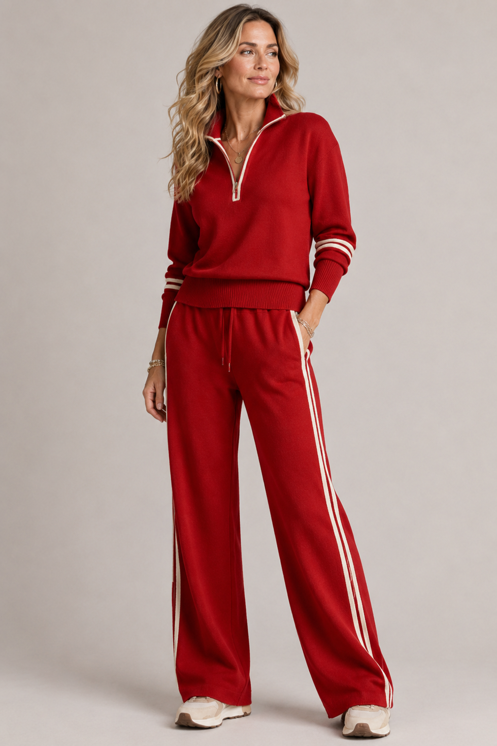Woman in the red set with cream zipper trim and side stripes, one hand in pocket, with beige sneakers. 4