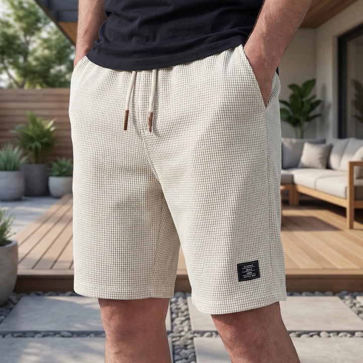 Model on a patio wearing cream waffle-textured shorts with a drawstring waist and a small woven label 2