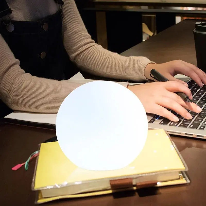 White orb lamp on a notebook beside a person typing on a laptop