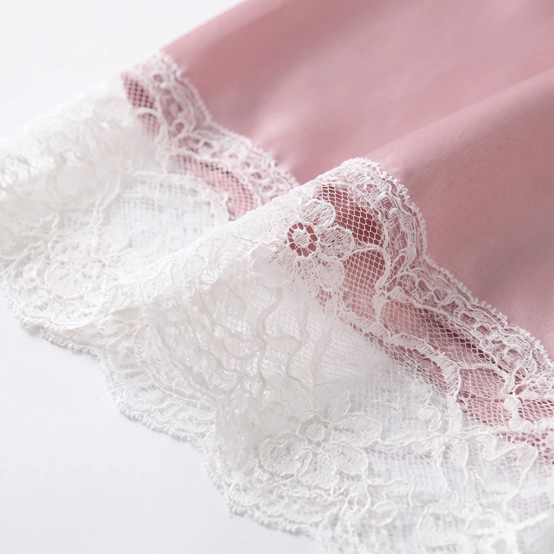 Close-up of delicate white floral lace trim sewn onto the hem of smooth pink satin fabric. 4