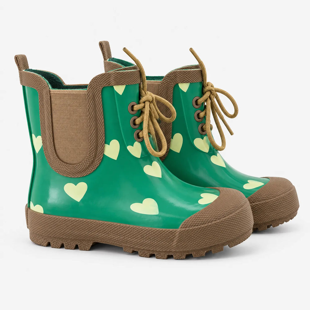 Pair of green rubber rain boots with pale heart print, brown elastic side panels, three-eyelet laces, pull tab and chunky lugged sole, shown on white. 2