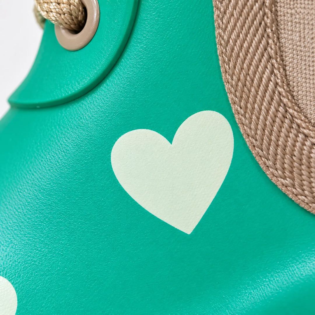 Close-up of a pale heart print on glossy green rubber, with a brown lace eyelet and woven elastic side panel edge. 6