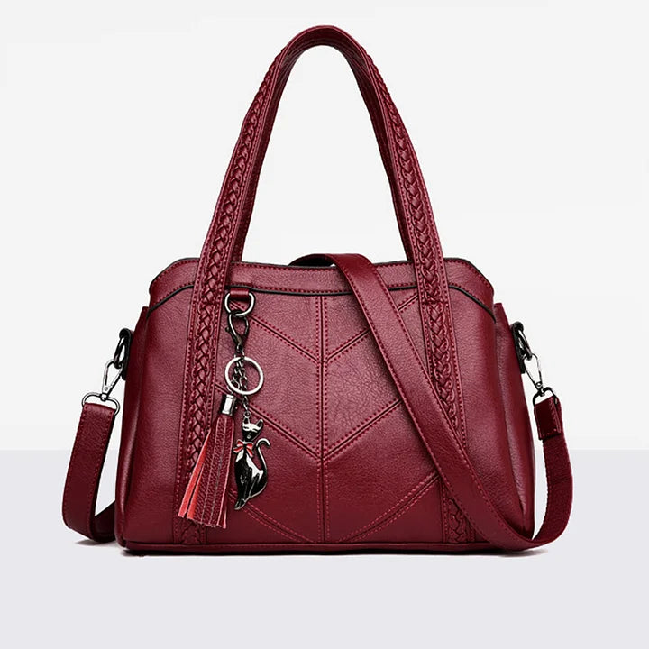 Red leather handbag front view with braided handles, chevron stitching, shoulder strap and charm.