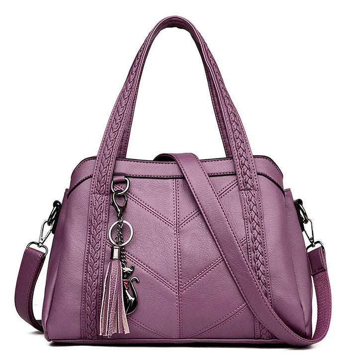 Lilac purple leather handbag front view with braided handles, a matching shoulder strap and a cat charm.