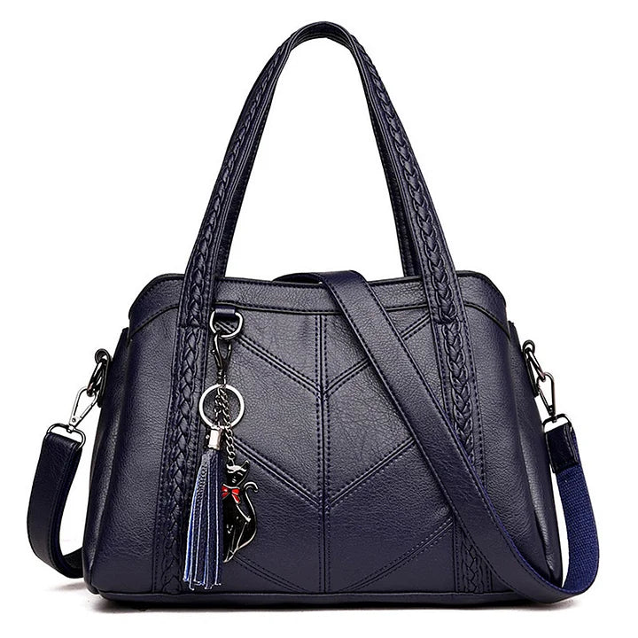 Navy blue leather handbag front view with braided handles, chevron stitching, a woven shoulder strap and a cat charm.