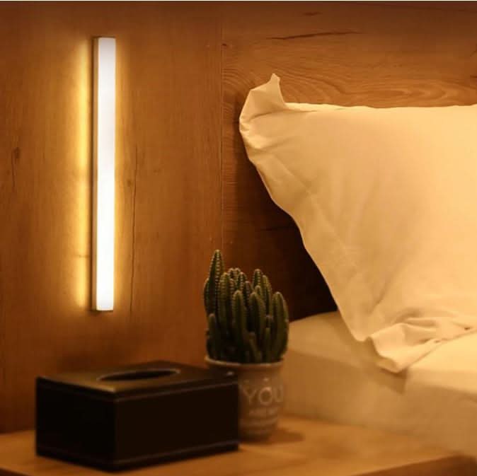 White motion sensor LED light bar shown as another view glowing on a wooden headboard wall.
