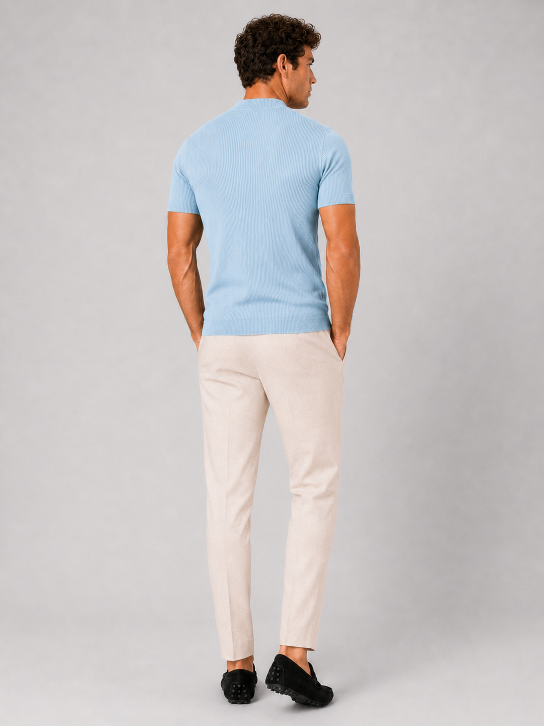 Back view of the men's light blue ribbed mock neck tee with cream trousers and black loafers.