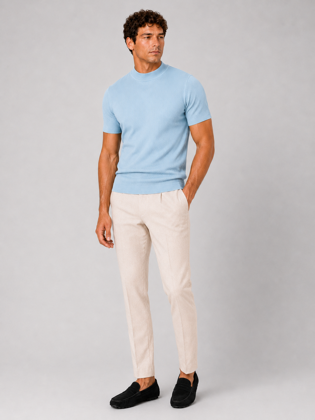 Men's light blue ribbed tee with cream pleated trousers and black suede loafers, front view.