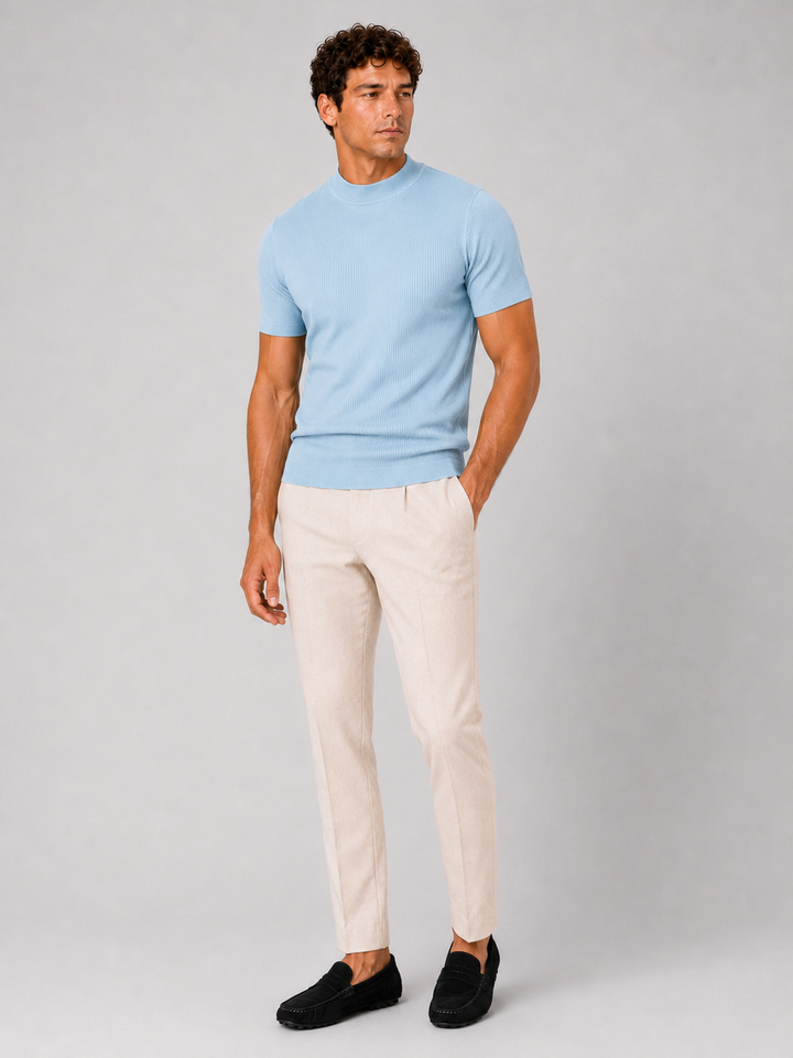 Men's light blue ribbed tee with cream pleated trousers and black suede loafers, front view.