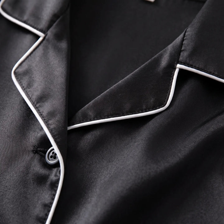Close-up of the notched collar with white piping and a gray button on the black satin shirt. 5