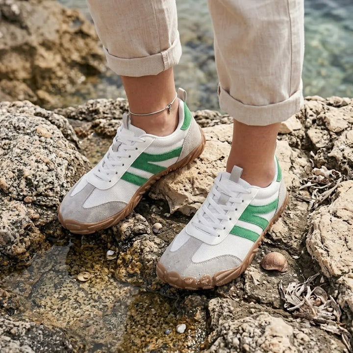 Woman wearing the white and green sneakers while standing on coastal rocks beside shallow water, with rolled linen pants and an ankle bracelet. 29
