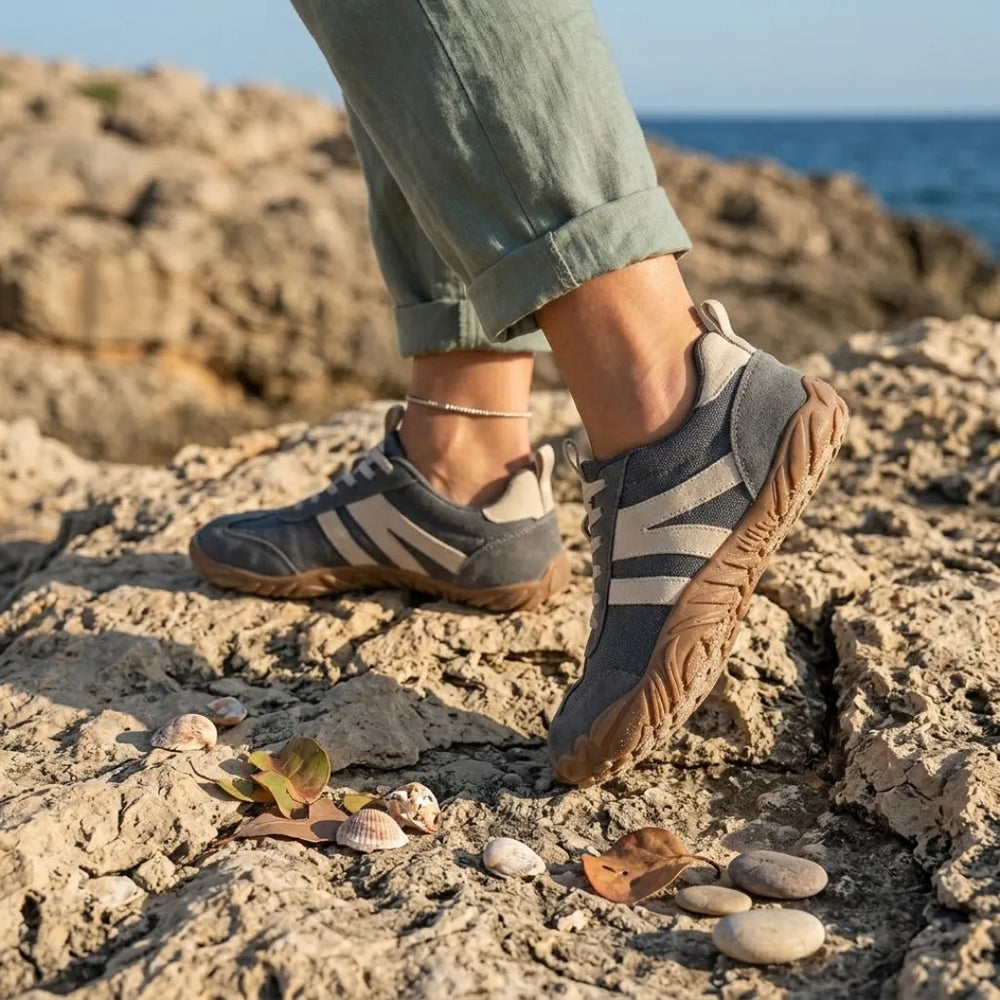 Lilia Women's Barefoot Shoes in gray worn on a rocky shoreline.