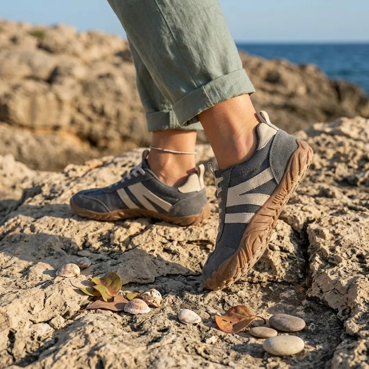 Lilia Women's Barefoot Shoes in gray worn on a rocky shoreline.