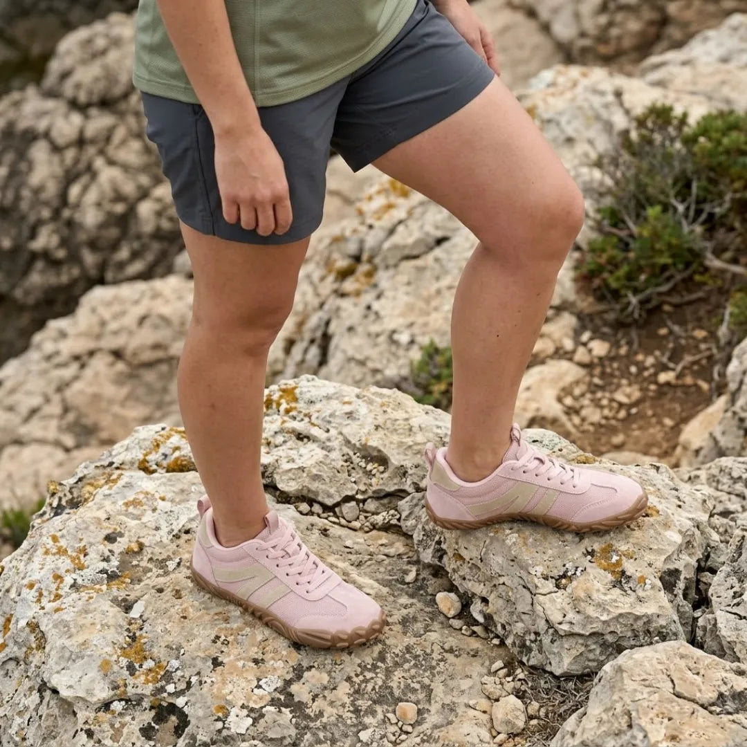 Woman wearing pink Lilia Women's Barefoot Shoes standing on a lichen-covered rock.