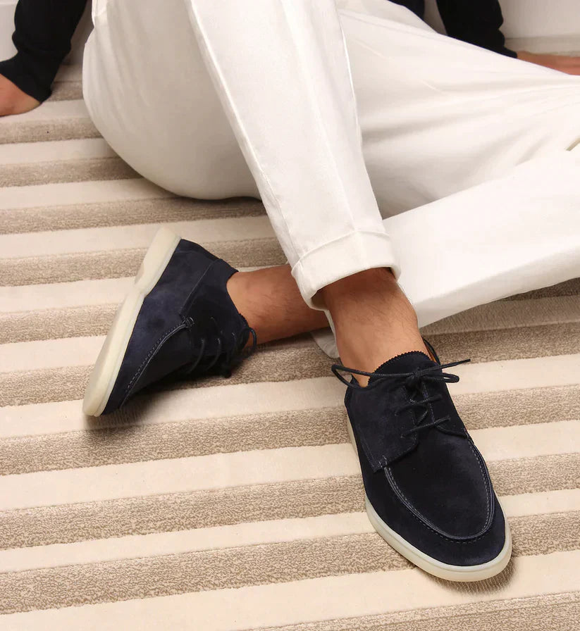 Men's blue leather lace-up shoes seen on a seated man with cuffed white trousers.