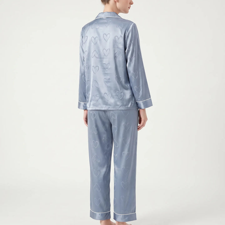 Back view of the blue satin pajamas on a model, showing the all-over heart pattern on the top and pants. 3