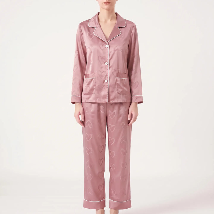 Front view of a model wearing the same heart-patterned satin pajama set in a dusty pink shade, with white piping. 6