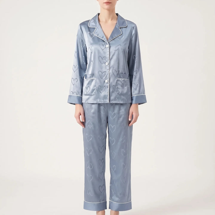 Front view of a model standing in the blue satin pajamas, with wide-cuffed sleeves and straight pants with white piping. 7