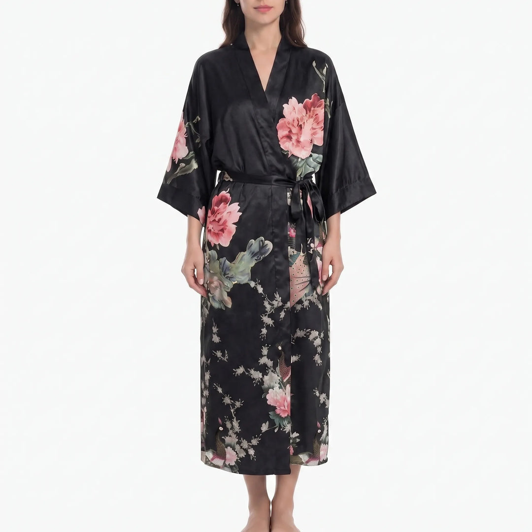 Model in a black satin kimono robe printed with large pink peonies, blossoming branches and peacocks, tied with a black belt. 11