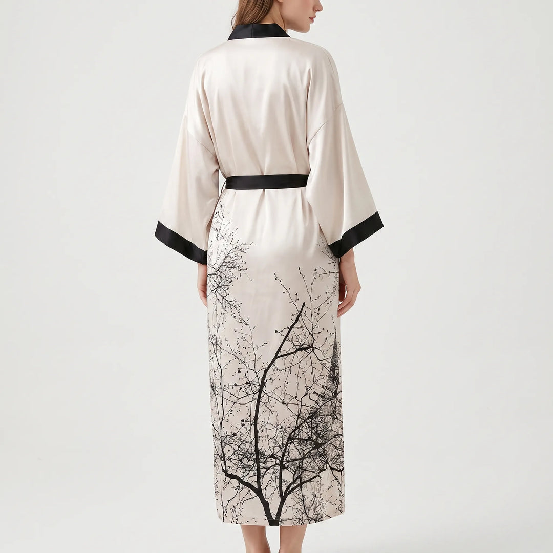 Back view of a blush satin kimono robe with black belt and cuffs, a large branch print covering the lower back. 3