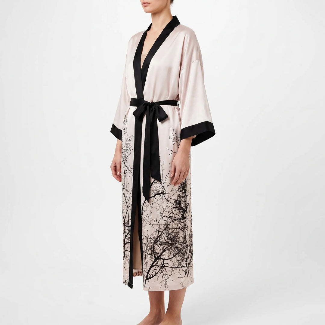 Side view of a blush satin kimono robe with black lapels and belt, branch print on the hem, front slit visible. 4
