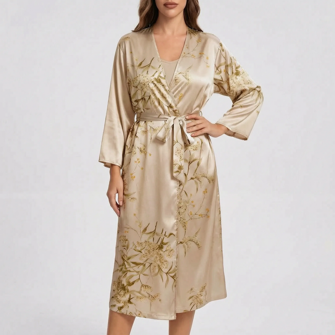 Model wearing the robe in champagne beige satin with a gold and olive floral print, belt tied, one hand on hip. 6