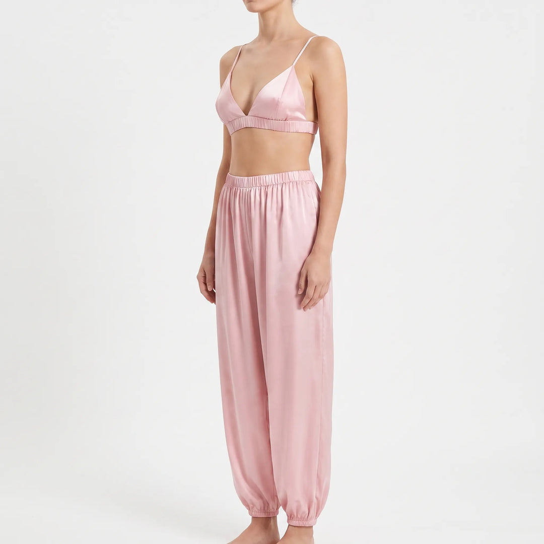 Three-quarter side view of model in the pink satin bralette and relaxed pants with gathered ankle cuffs. 4
