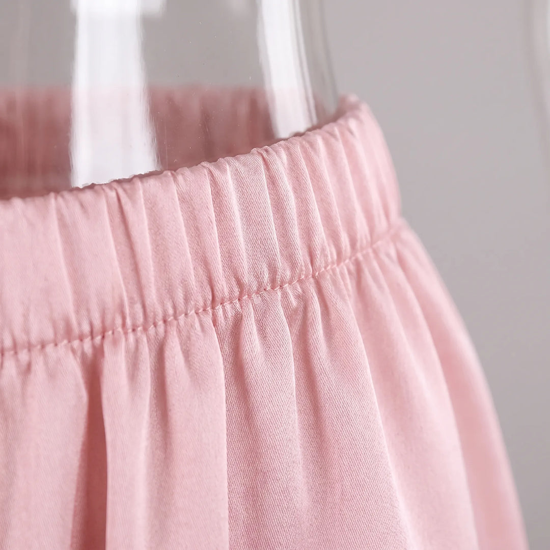 Close-up of the pink satin pants' gathered elastic waistband and stitching, photographed against a clear glass object. 5