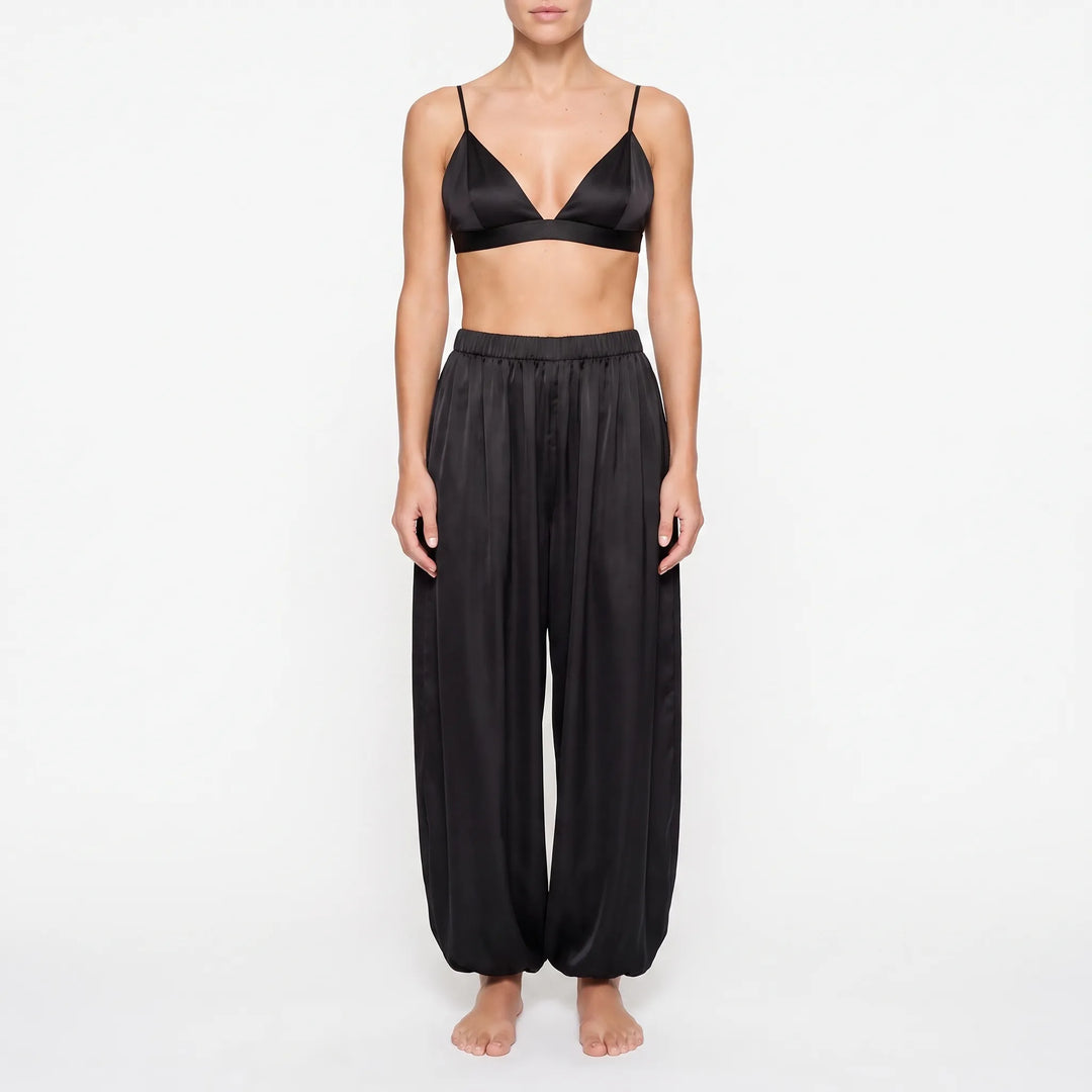 Front view of model in the black satin version: triangle bralette and loose pants with elastic ankle cuffs. 6