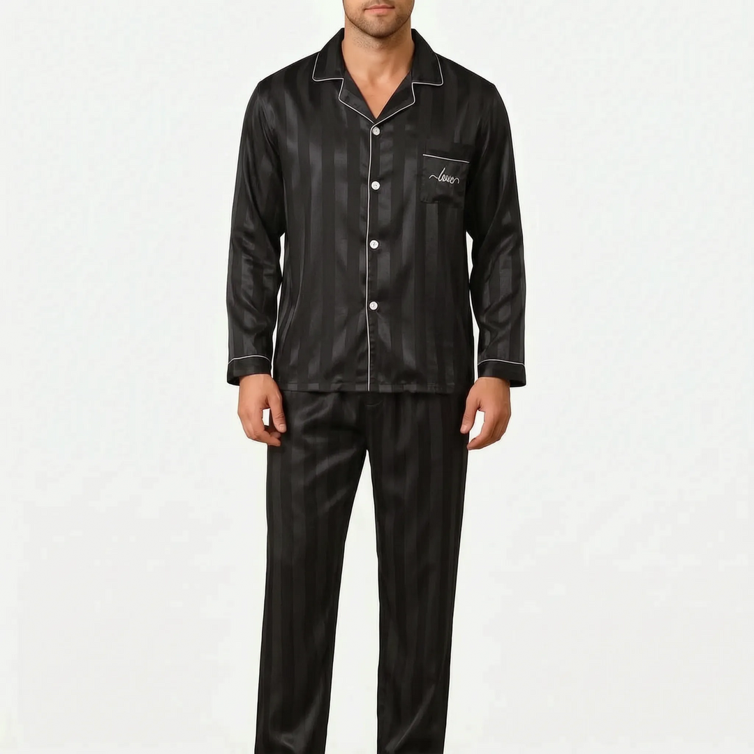 Model wearing the striped satin pajama set in black with white piping and embroidered chest pocket, front view. 8