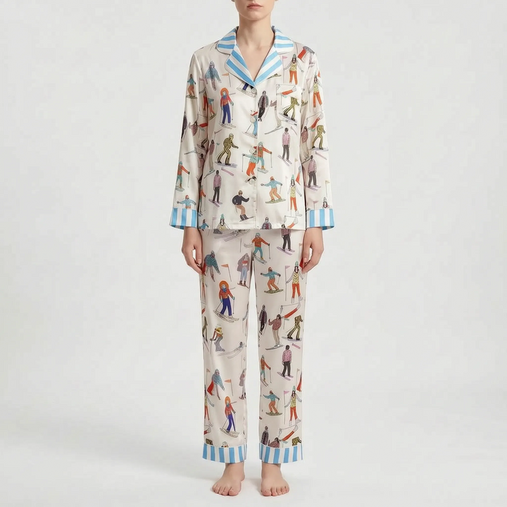 Front view of the cream skier print pajama set with blue striped collar, cuffs and hems, worn by a standing model. 11