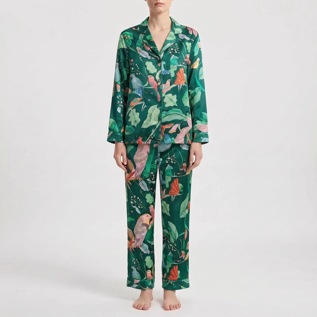 Pajama set in a different print: deep green with colorful birds and large leaves, worn by a model standing barefoot. 8
