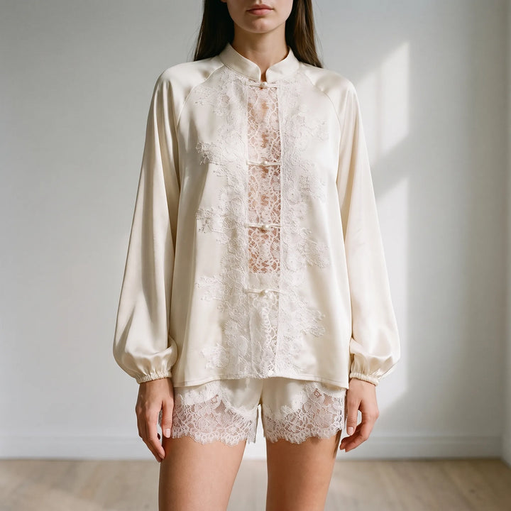 Model standing in a bright room wearing the cream satin top with floral lace panel and pearl buttons, plus lace-trimmed shorts. 1