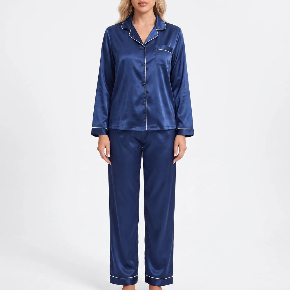 Front view on a plain background of a model in navy satin pajamas with white piping, chest pocket and button front. 2