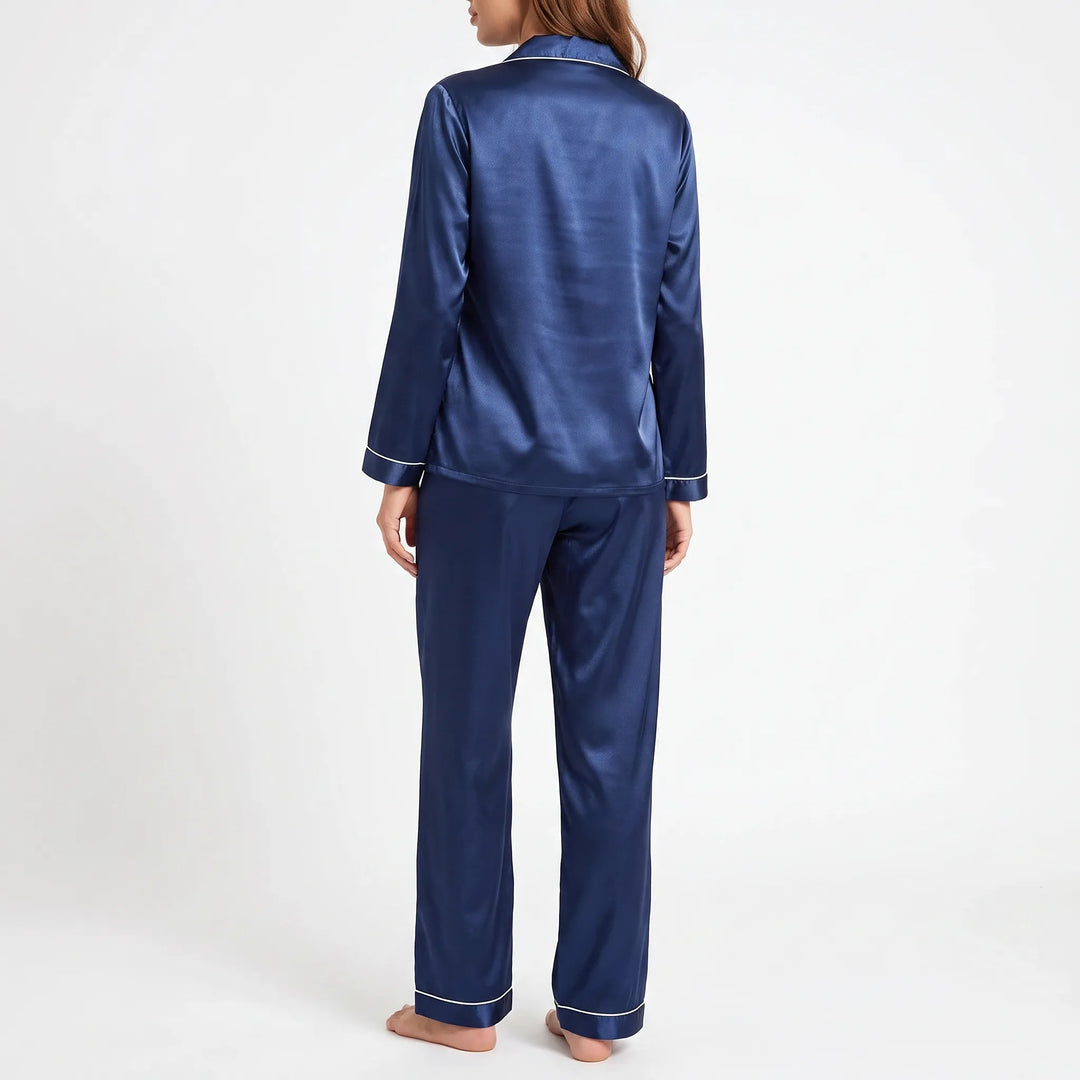 Back view of a model wearing the navy satin pajama top and pants, showing the smooth back and piped cuffs. 3