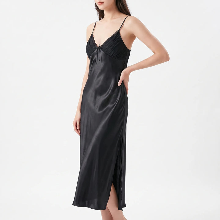 Model with hand on hip wears the long satin nightdress in black, with lace-edged pleated bodice and side slit. 10