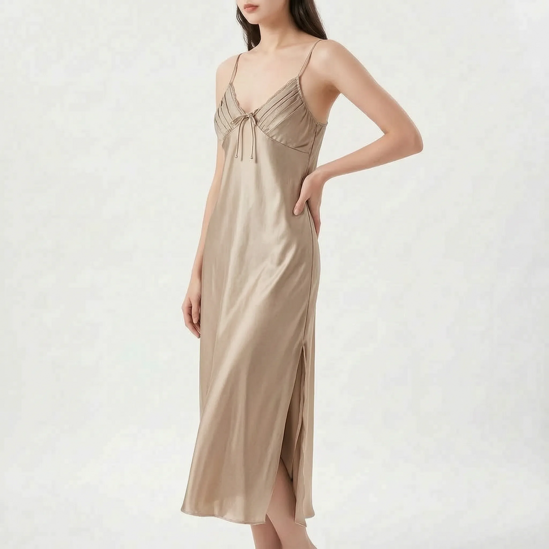 Model with hand on hip wears the long satin nightdress in champagne beige, with pleated bodice and side slit. 6