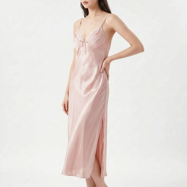 Model with hand on hip wears the long satin nightdress in soft blush pink, with pleated bodice and side slit. 7