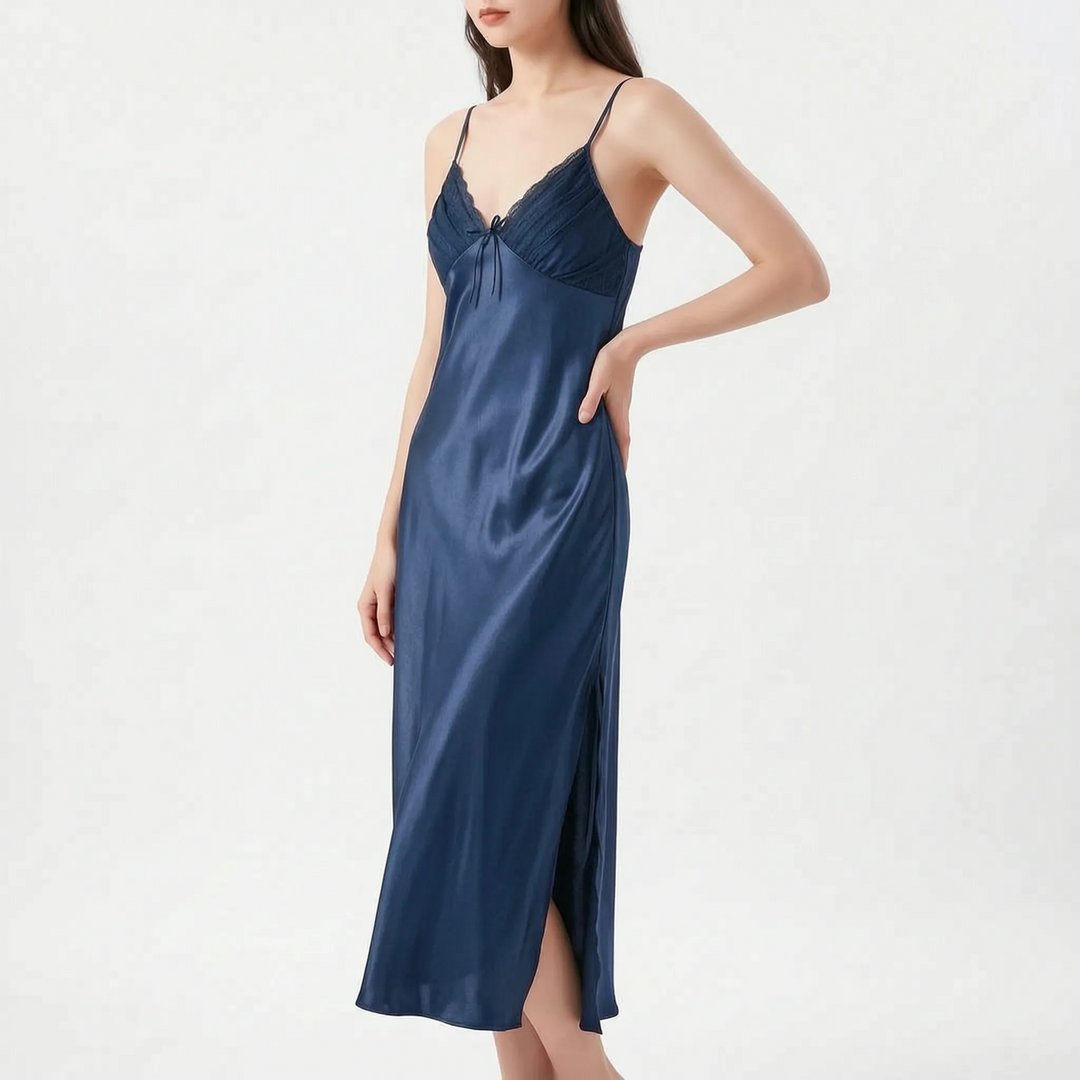 Model with hand on hip wears the long satin nightdress in navy blue, with lace-edged pleated bodice and side slit. 9
