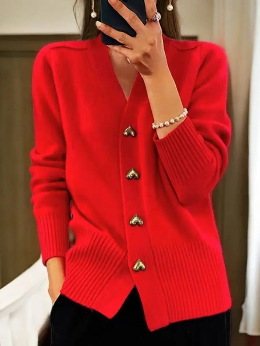 Woman in a bright red wool cardigan with gold heart buttons and ribbed trim, a pearl bracelet, and black pants.