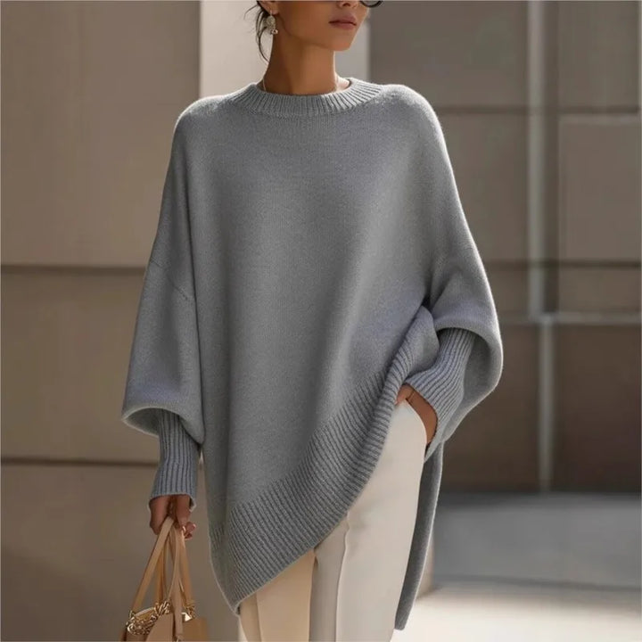Gray oversized knit sweater with ribbed cuffs and asymmetric hem, worn with white trousers and a beige handbag 2