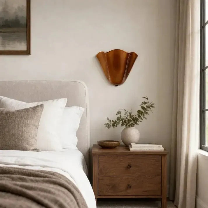 Amber-brown ruffled sconce mounted above a wooden nightstand with books and a vase in a bright bedroom. 3