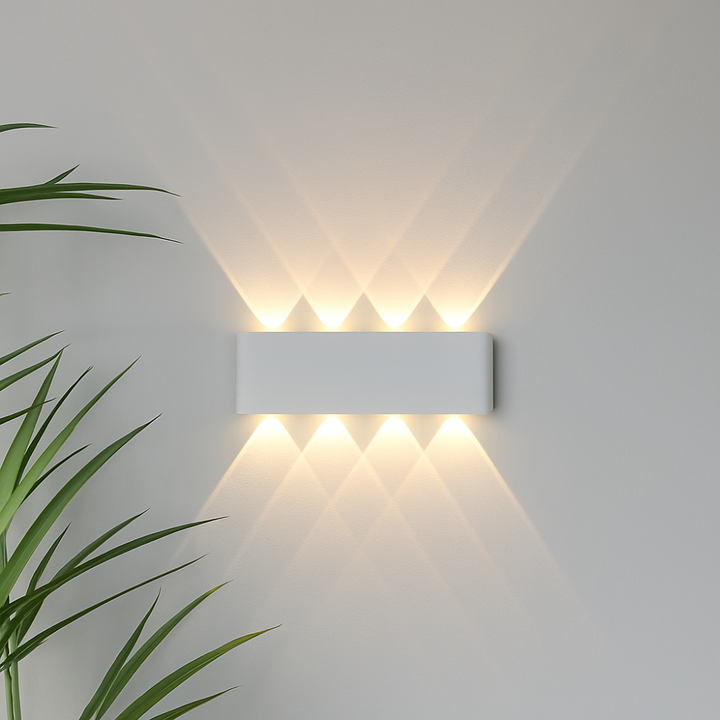 Long white wall light detail on a pale wall, shooting four warm beams upward and four downward in overlapping triangles.