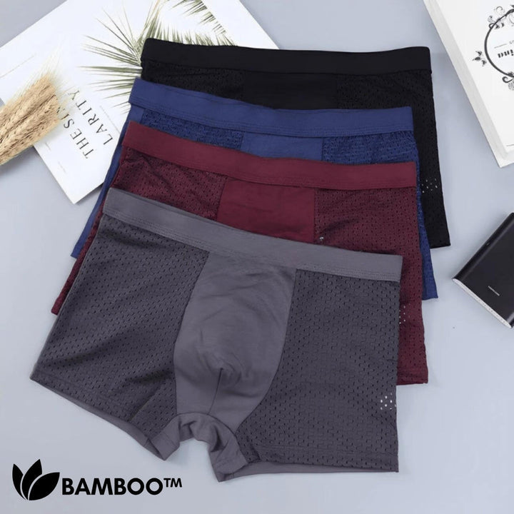 Flat lay of four stacked boxer briefs in black, blue, burgundy and gray with mesh side panels on a light surface. 3