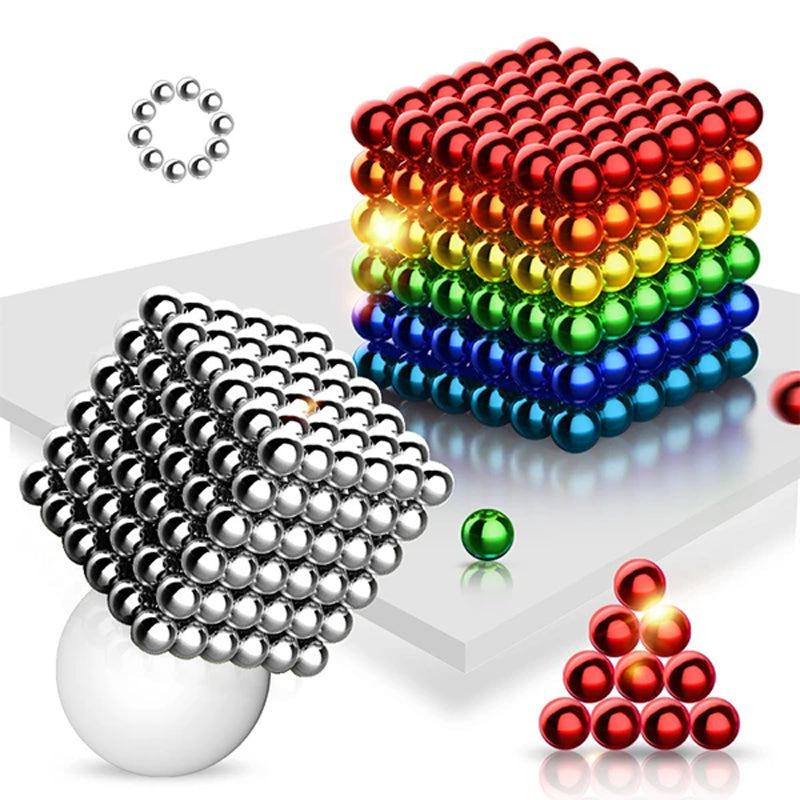 Silver magnetic ball cube beside a rainbow cube, with a ring of balls, a red pyramid and a loose green ball.