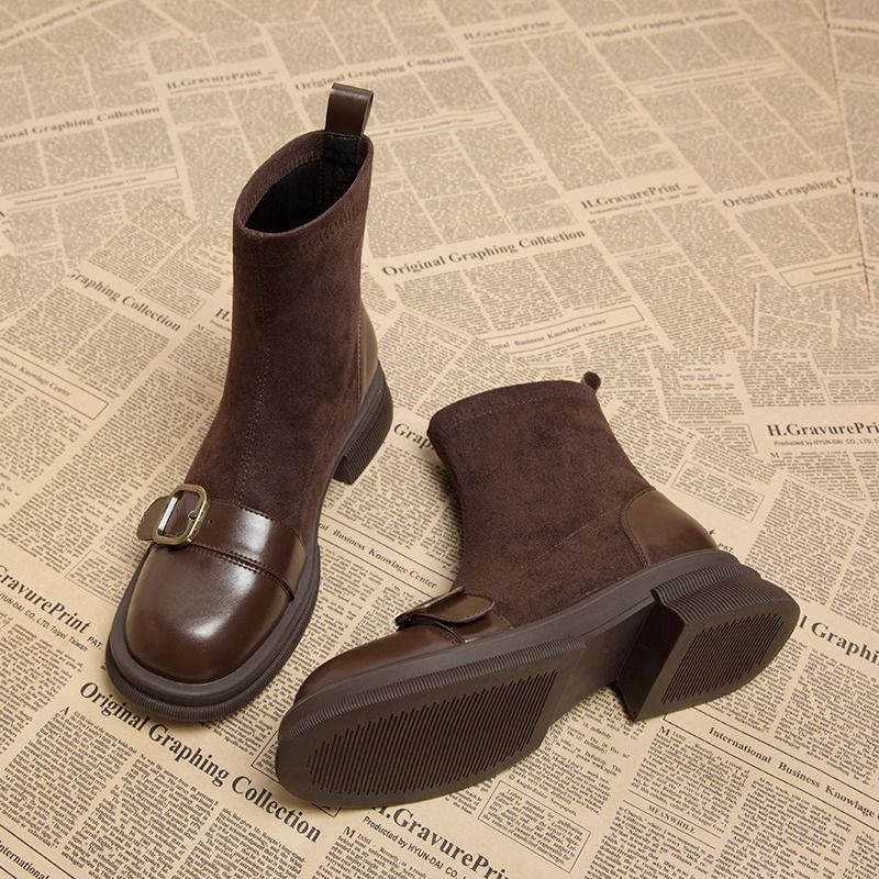 Pair of brown suede ankle boots with glossy leather toe caps and buckle straps, one turned to show the ridged sole.